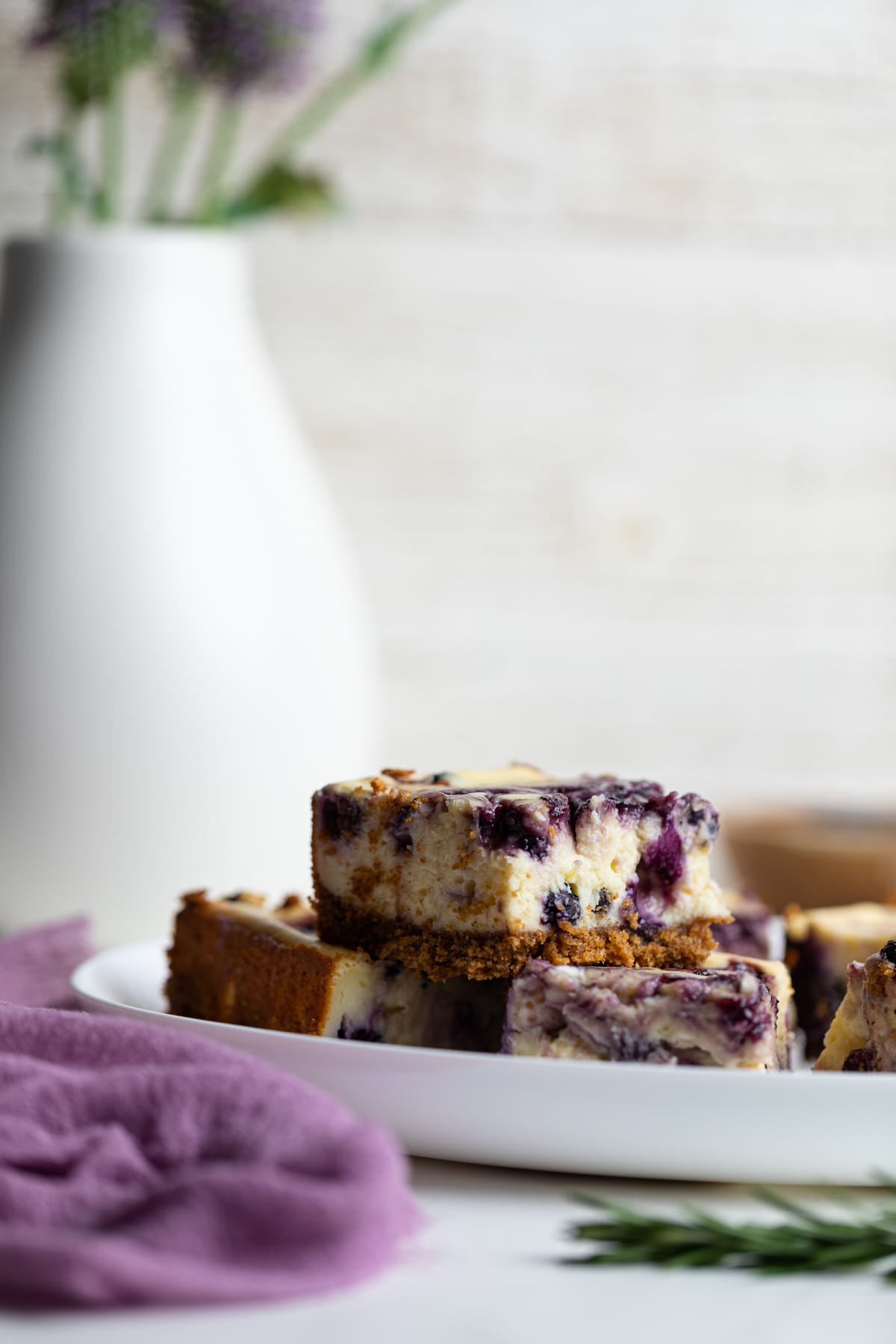 Lemon Blueberry Cheesecake Bars on a white plate with flowers in the background.