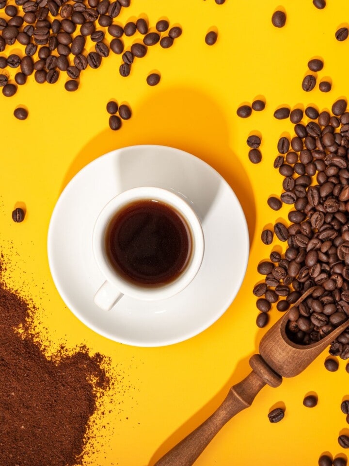 Black coffee in white cup on yellow background with beans.