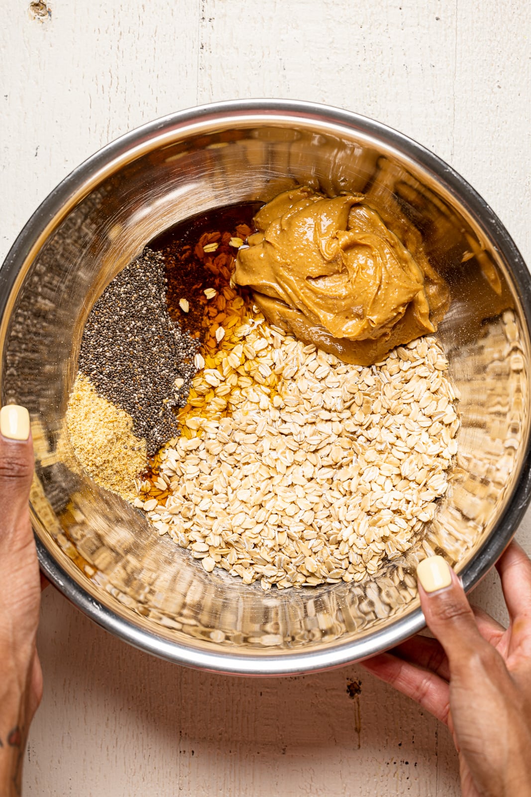All ingredients for protein balls in a large silver bowl being held.