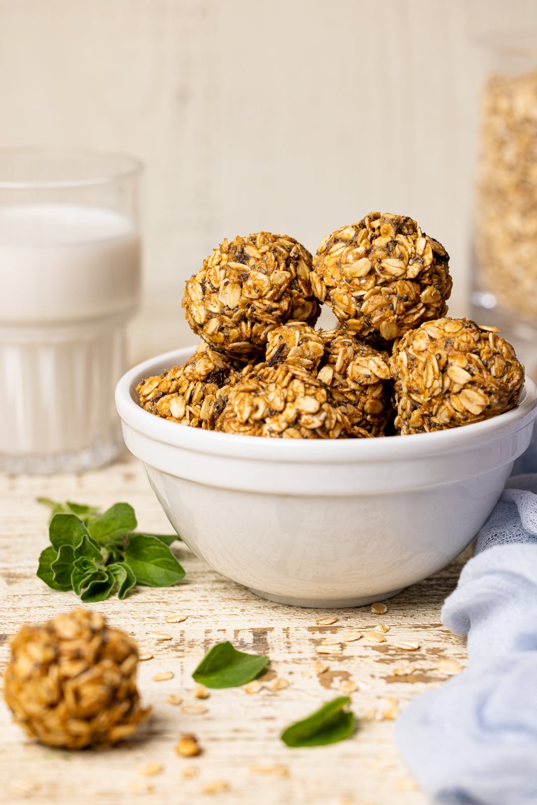 Protein balls in a white bowl stacked on a white wood table with a glass of milk and oats.