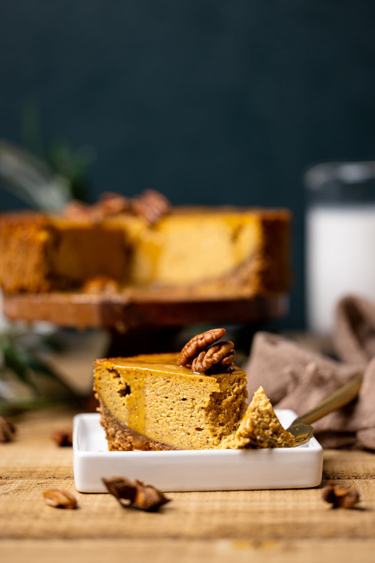 Slice of Caramel Pumpkin Cheesecake with a Pecan Crust next to a fork with a piece of the pie