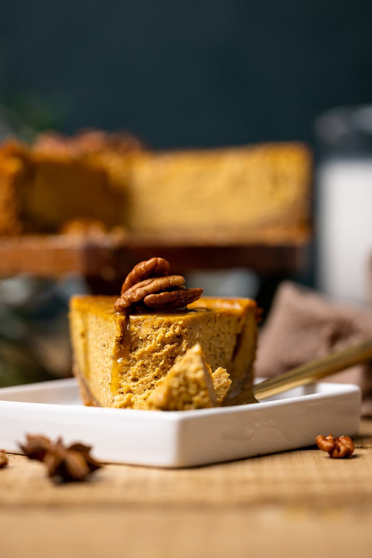 Slice of Caramel Pumpkin Cheesecake with a Pecan Crust next to a fork with a piece of the pie