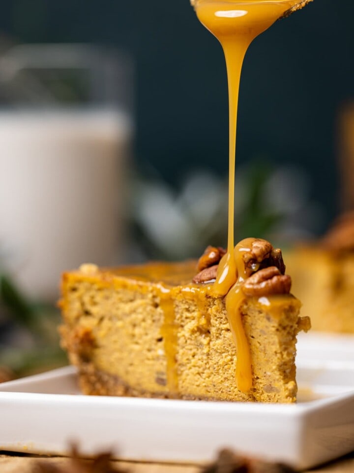 Slice of Caramel Pumpkin Cheesecake with a Pecan Crust being drizzled with caramel