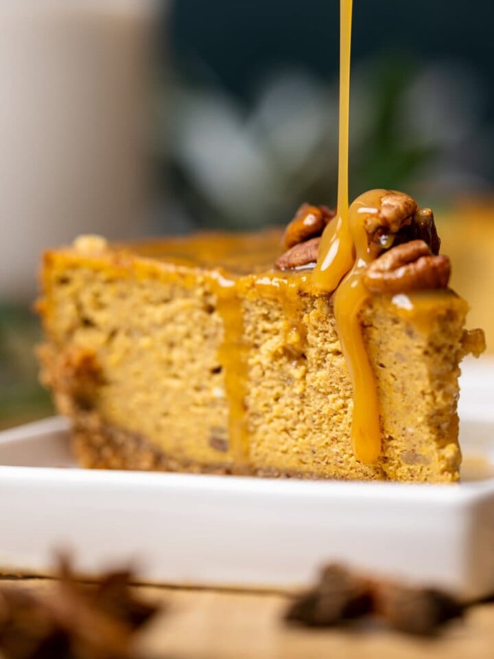 Slice of Caramel Pumpkin Cheesecake with a Pecan Crust being drizzled with caramel