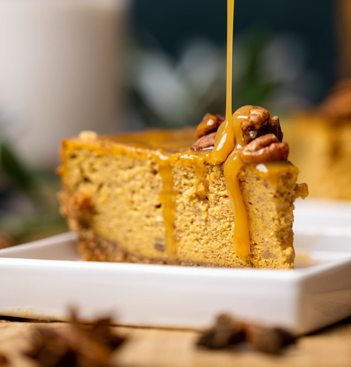 Slice of Caramel Pumpkin Cheesecake with a Pecan Crust being drizzled with caramel