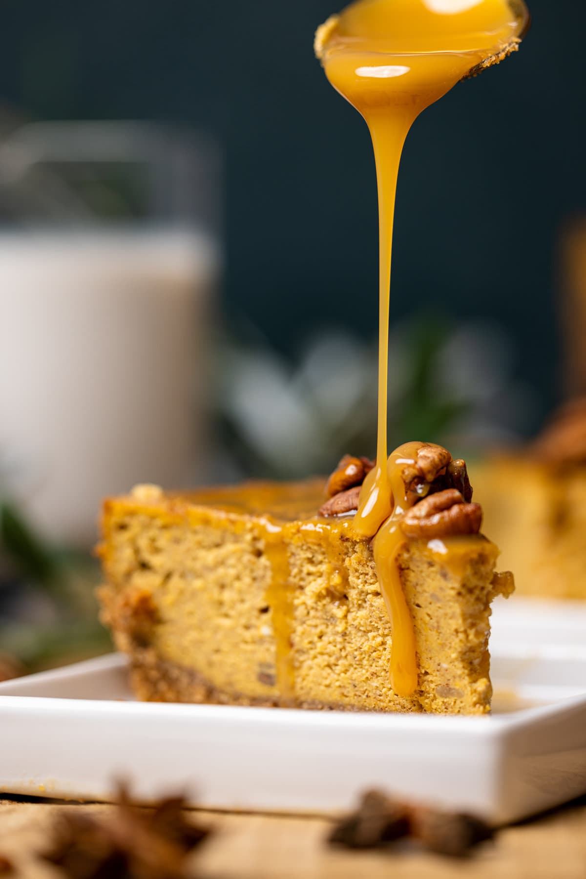 Slice of Caramel Pumpkin Cheesecake with a Pecan Crust being drizzled with caramel