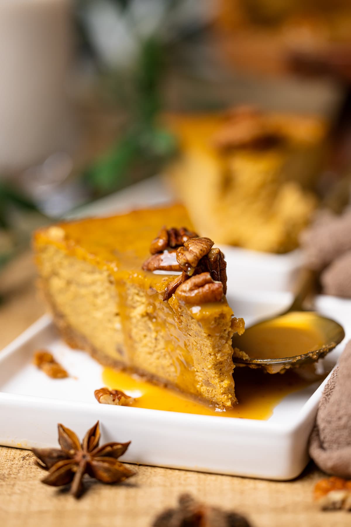 Slice of Caramel Pumpkin Cheesecake with a Pecan Crust next to a spoon of caramel