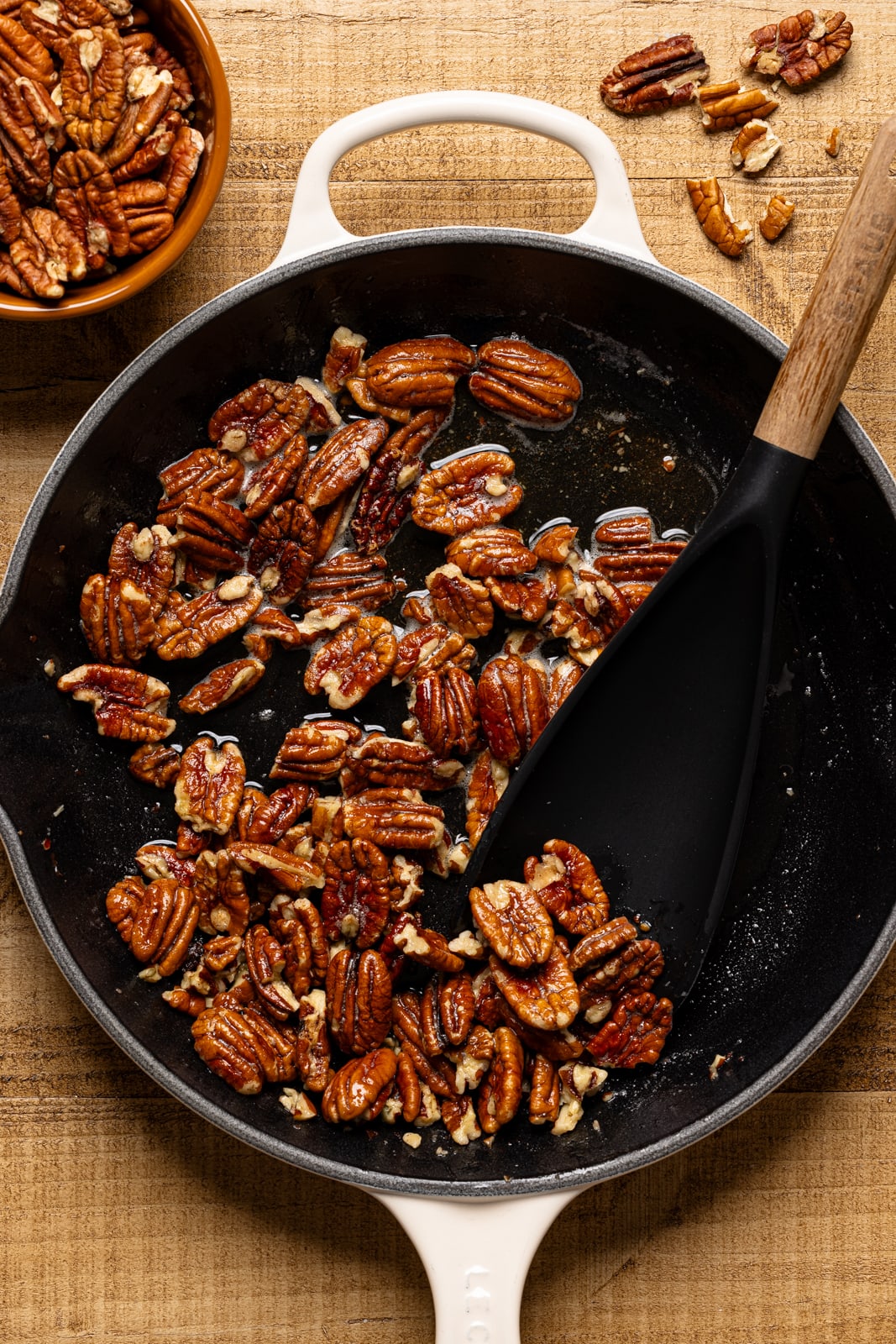 Pecan mixture in a white skillet on a brown wood table.