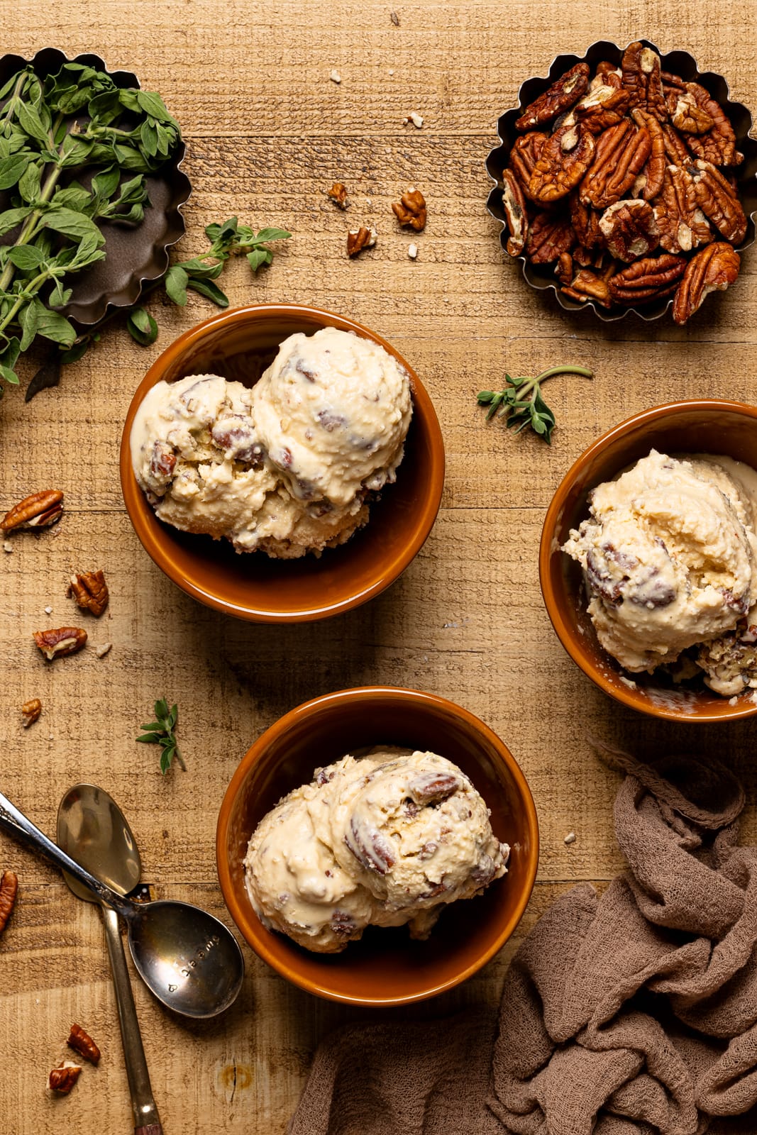 Three bowls of ice cream with pecans and two spoons.