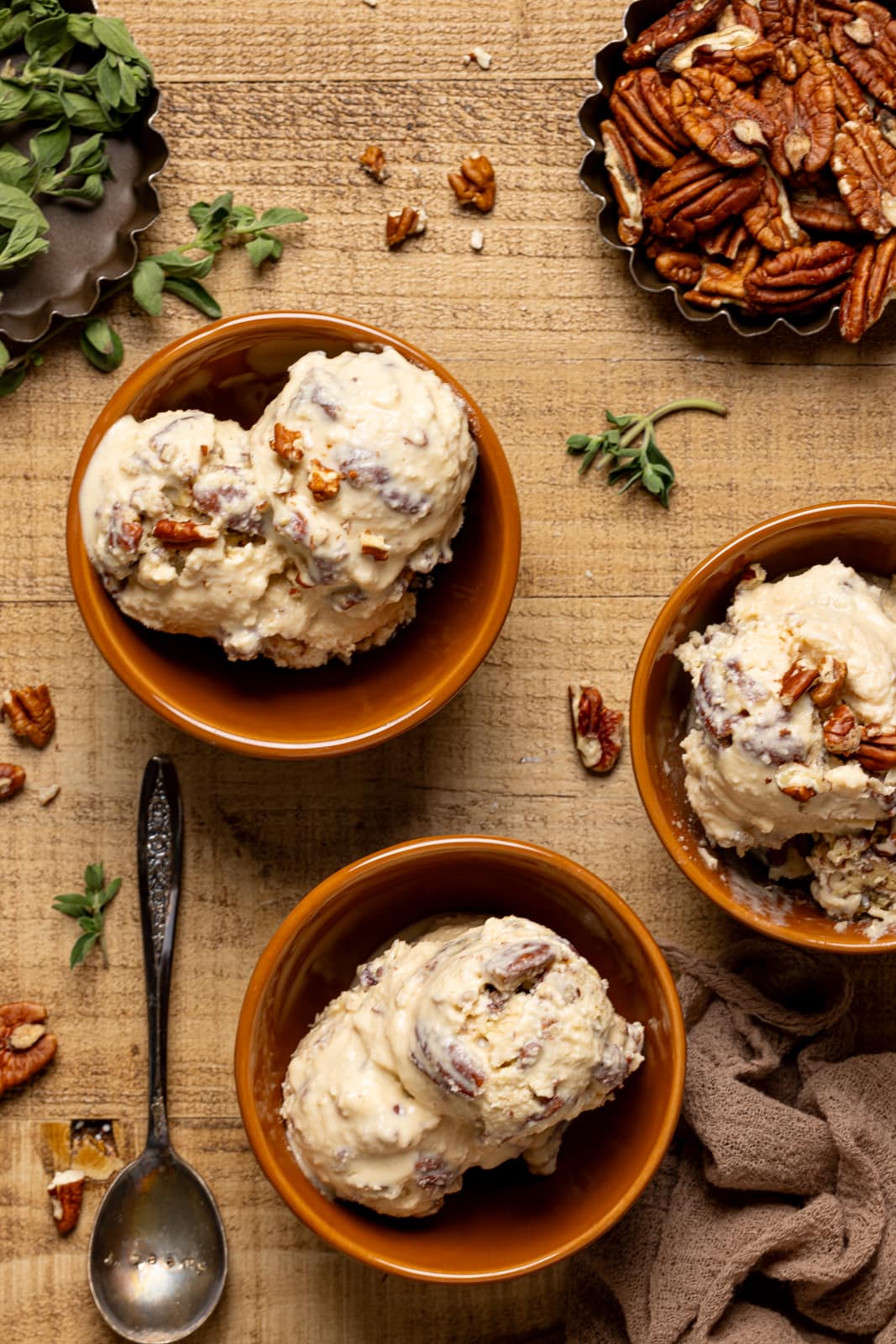 Up close shot of ice cream with pecans and spoon on a brown wood table.