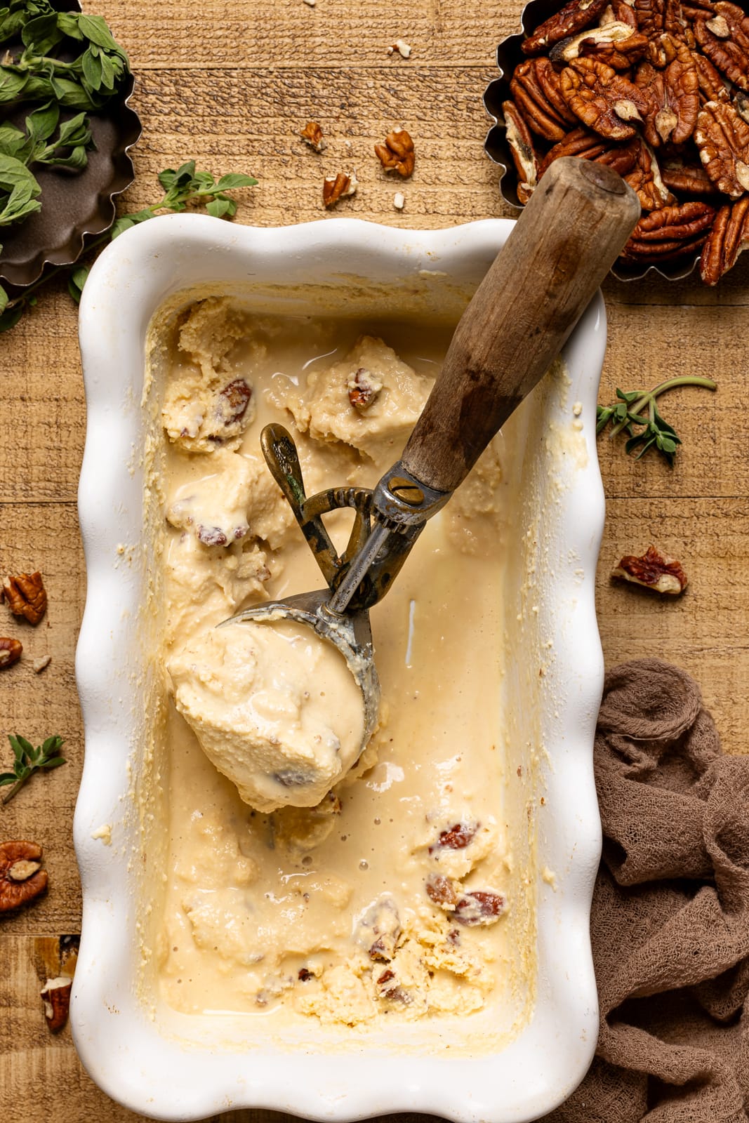 White pan with ice cream scoop and ice cream with chopped pecans.