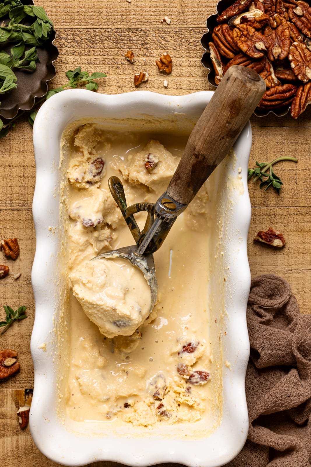 White pan with ice cream scoop and ice cream with chopped pecans.