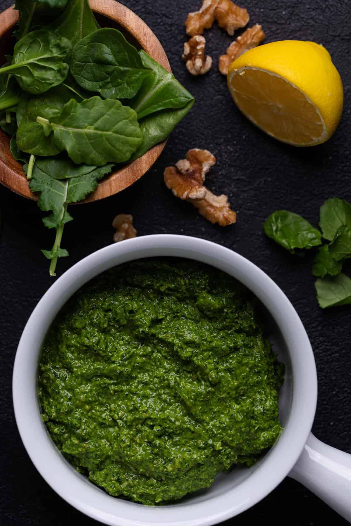 Bowl of pesto on a table with pesto ingredients.