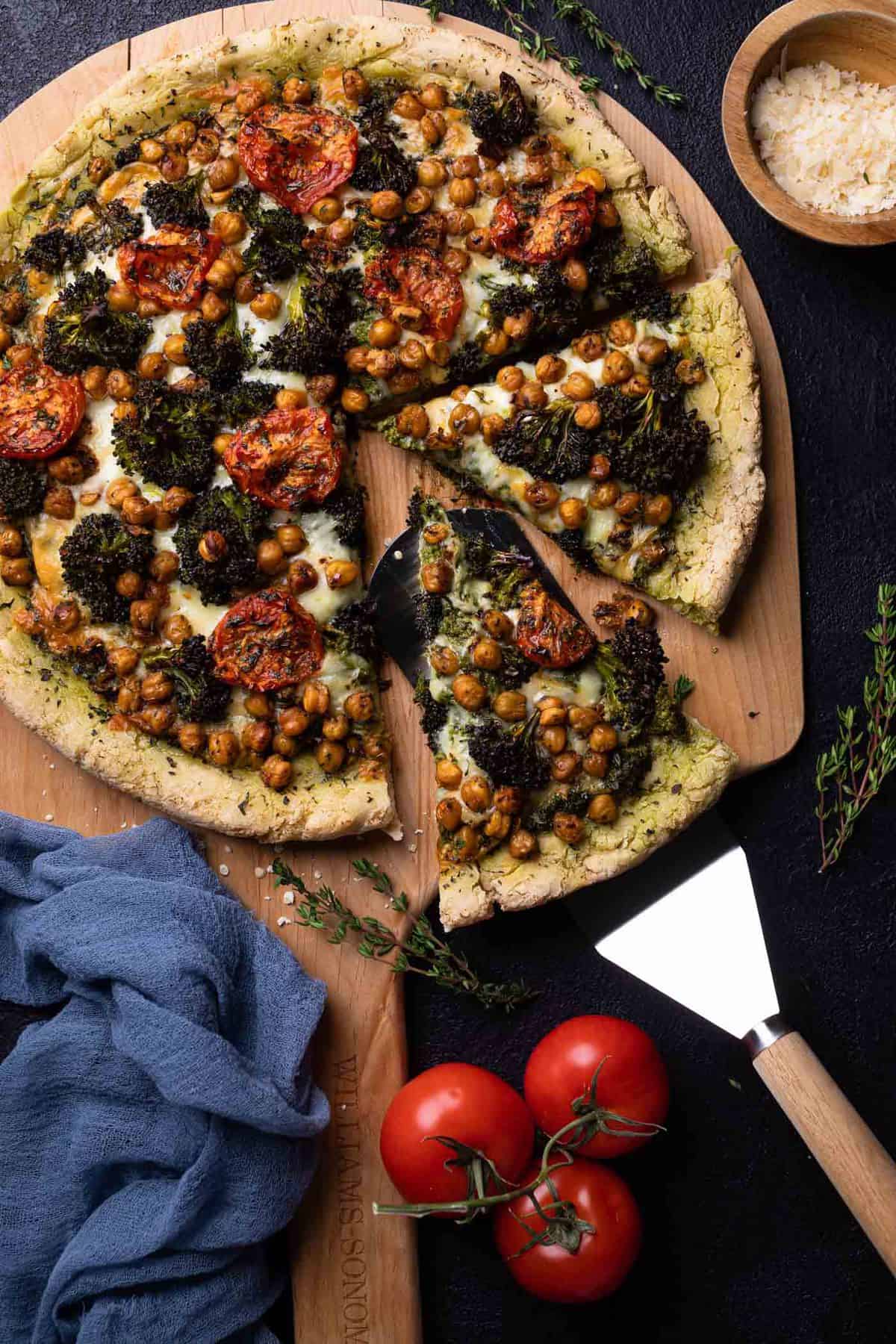 Partially-sliced Chickpea and Veggie Gluten-Free Pesto Pizza on a wooden board.