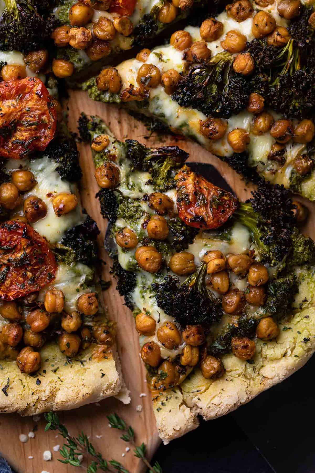 Slice of Chickpea and Veggie Gluten-Free Pesto Pizza on a wooden board.