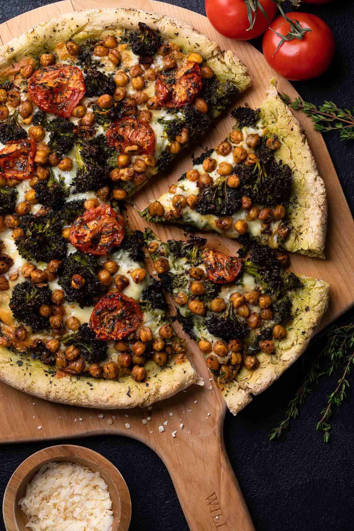 Wooden board with a partially-sliced Chickpea and Veggie Gluten-Free Pesto Pizza.