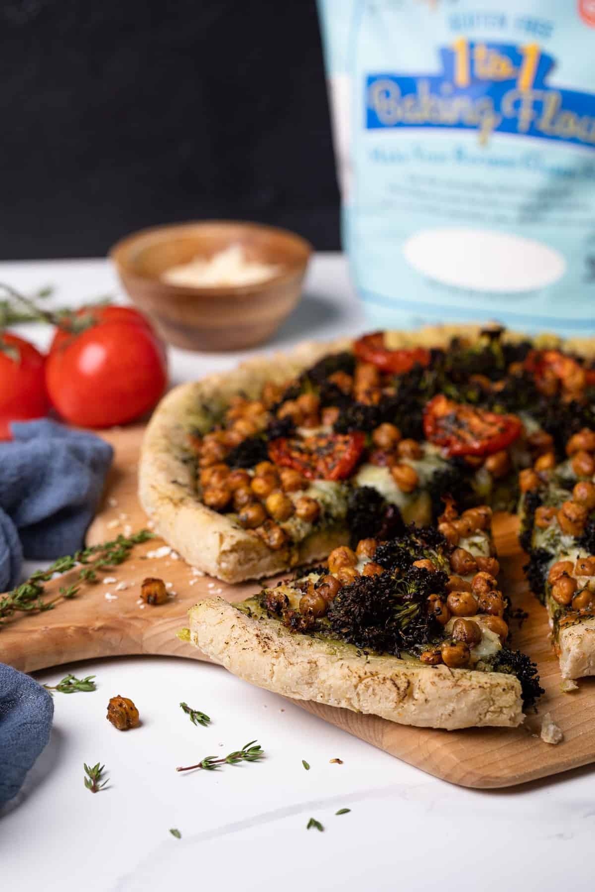 Chickpea and Veggie Gluten-Free Pesto Pizza on a table with pizza ingredients.