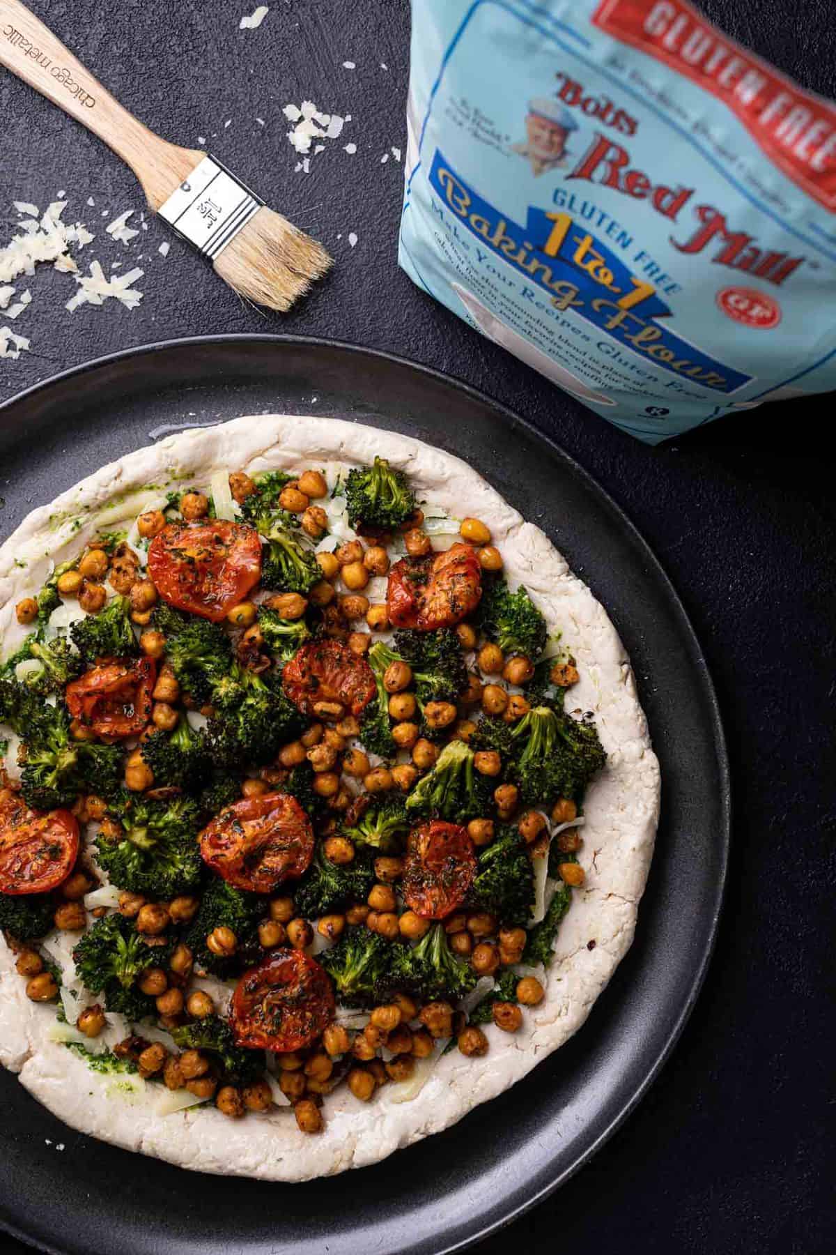 Uncooked Chickpea and Veggie Gluten-Free Pesto Pizza with a bag of Bob\'s Red Mill gluten-free flour.