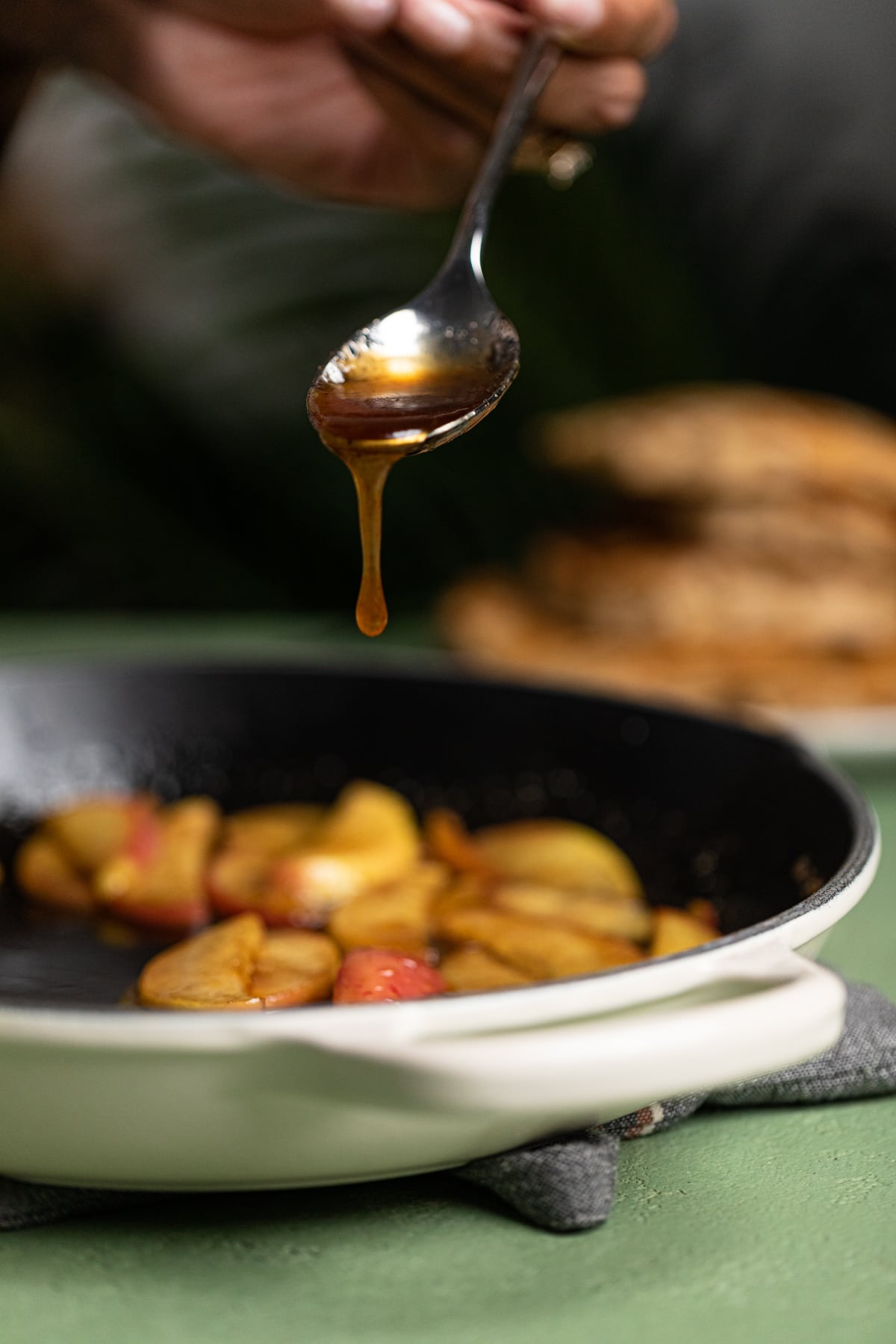 Spoon dripping with sauce from caramelizing apples