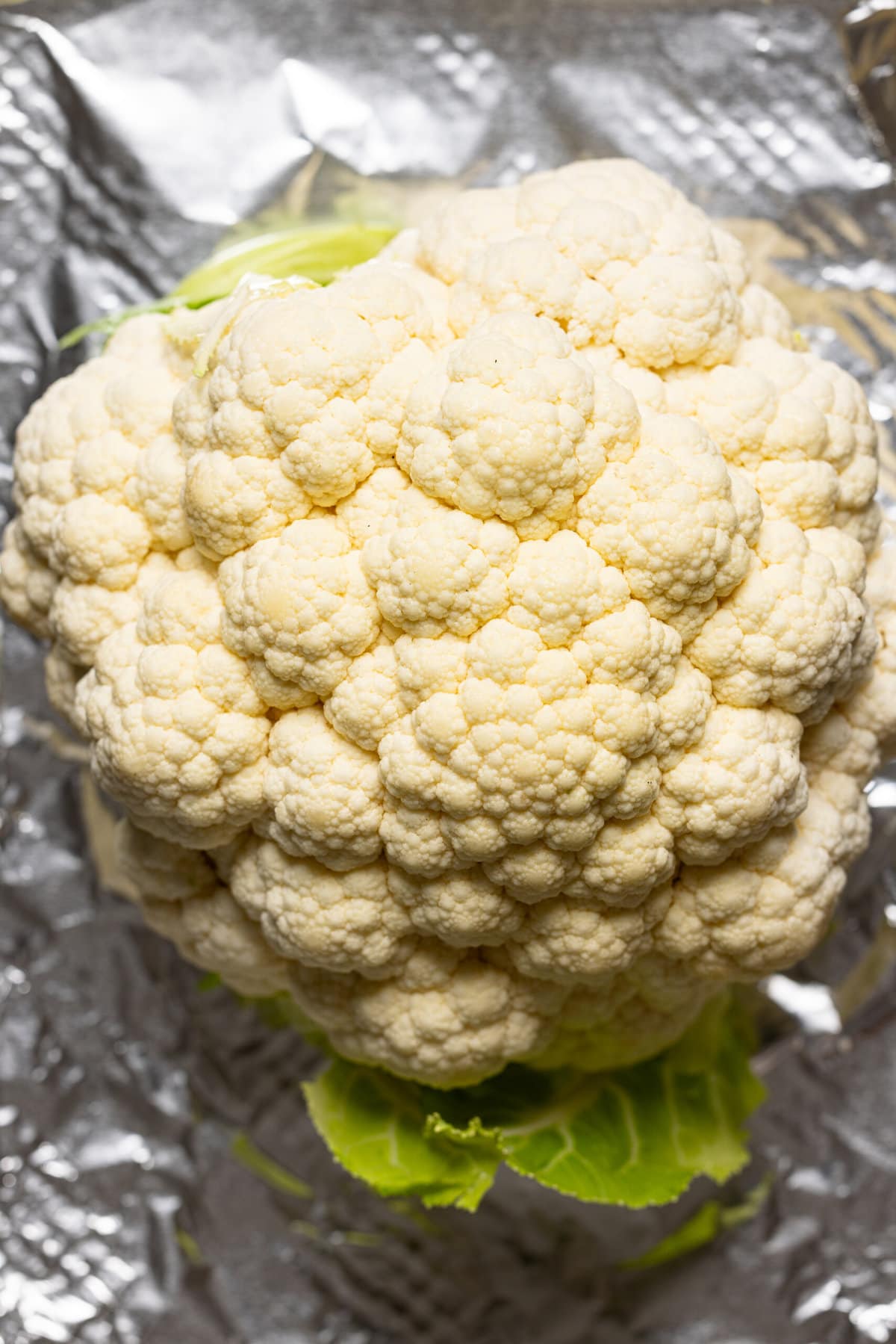 Whole cauliflower on a baking sheet lined with foil paper.