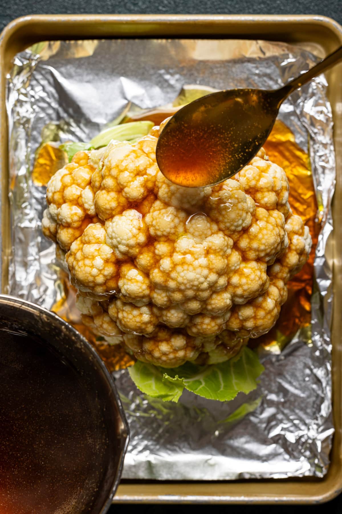 Sauce being spooned unto cauliflower. 