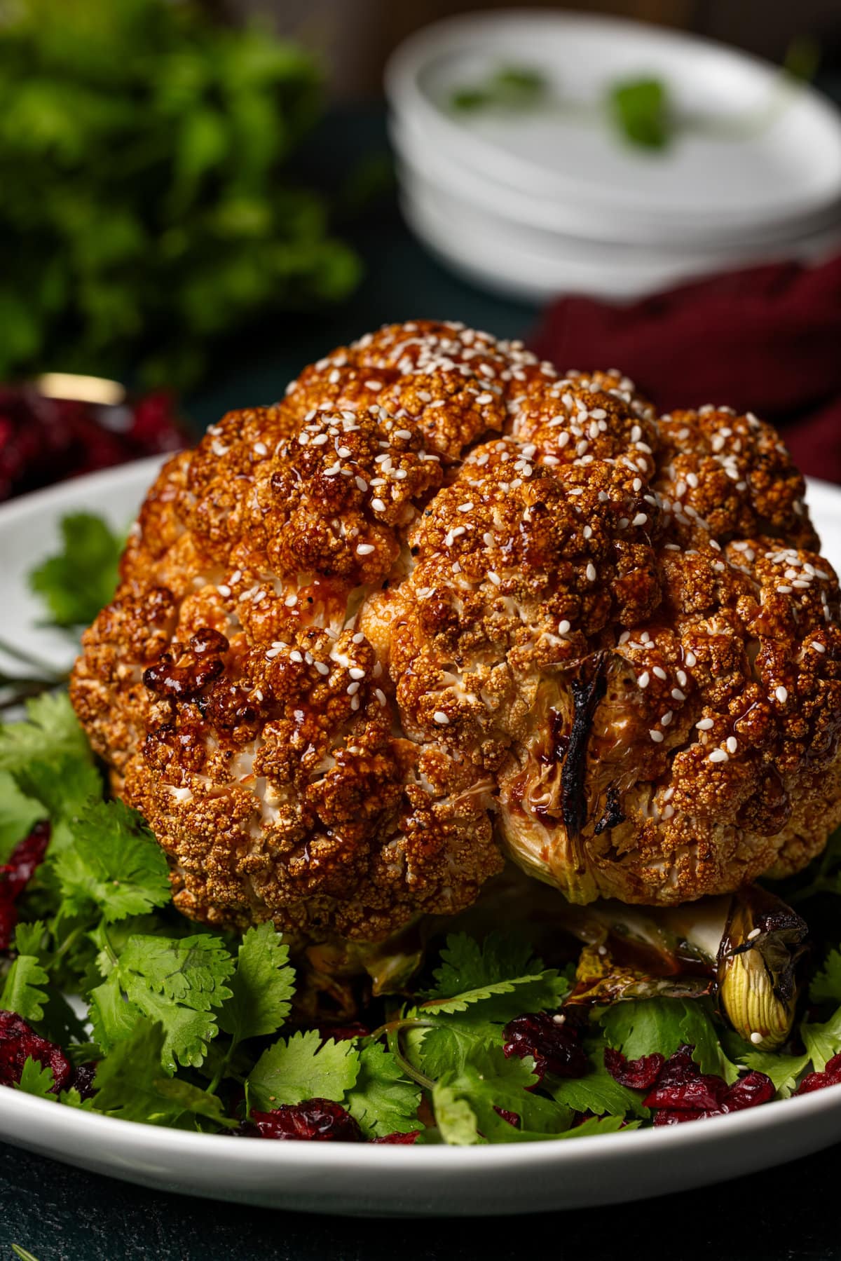 Side view of cauliflower on a white platter with garnish and cranberries. 