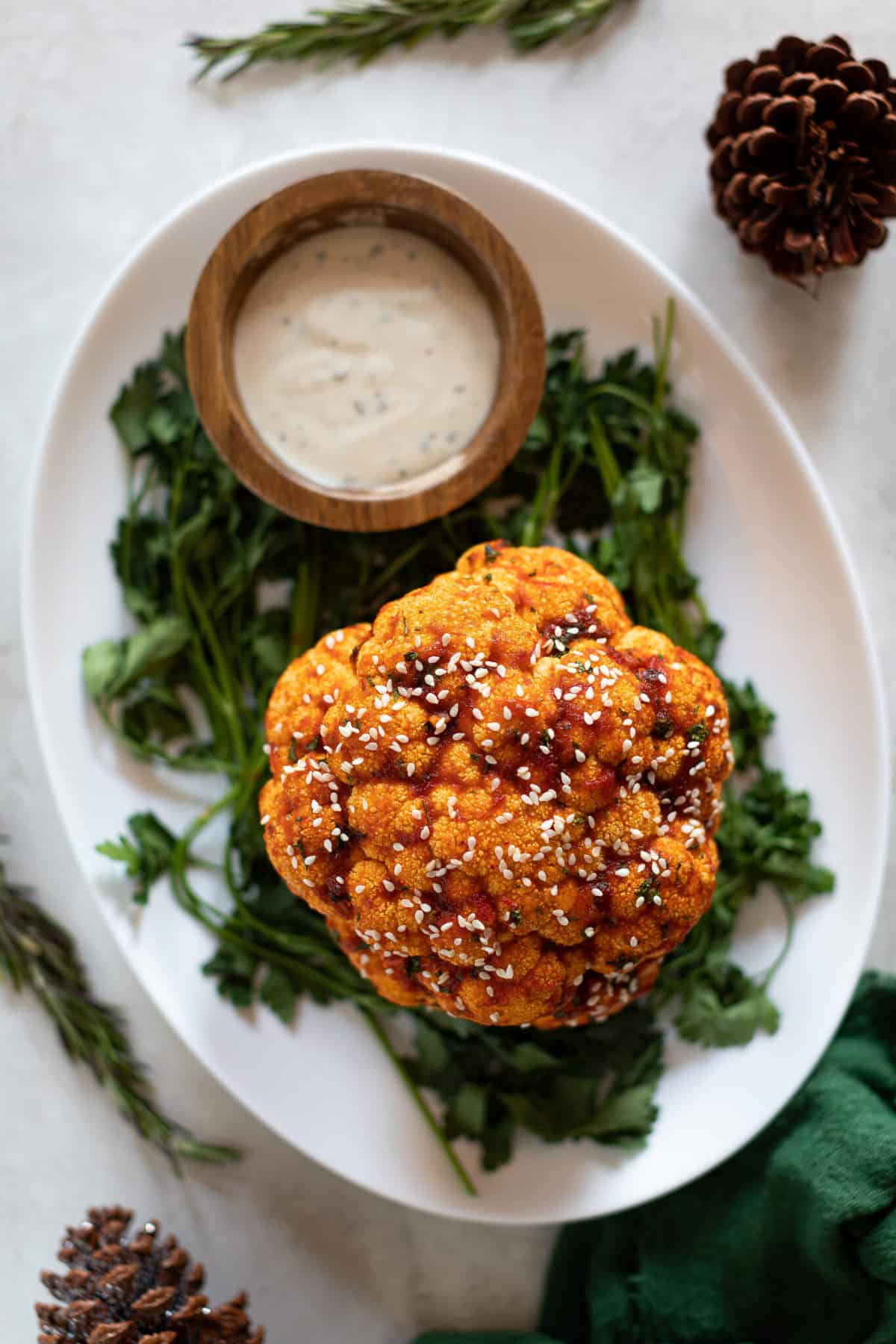 Sticky Teriyaki and Maple Whole Roasted Cauliflower on a white plate with greens and dip