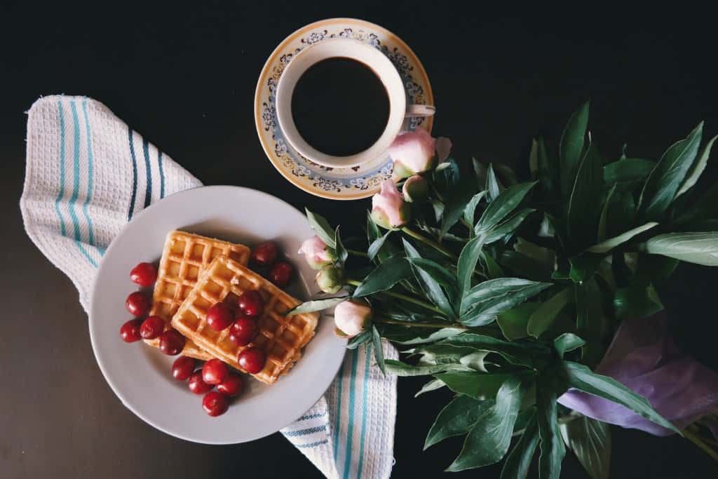 Plate of waffles next to a mug and flowers.