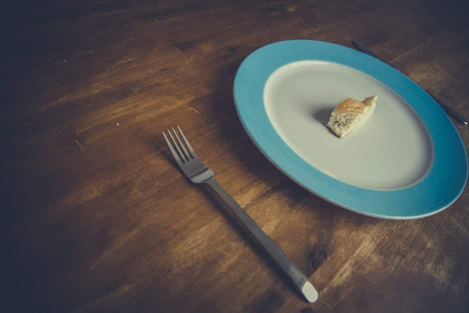 Mostly empty plate and a fork on a wooden table.