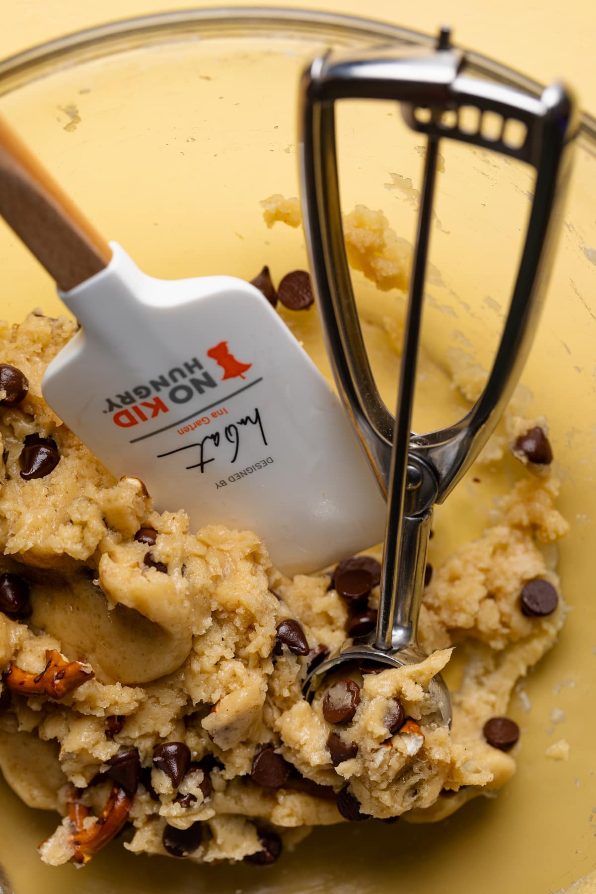 Spatula and dough scoop in a bowl of Vegan Chocolate Chip and Pretzel Cookie dough.