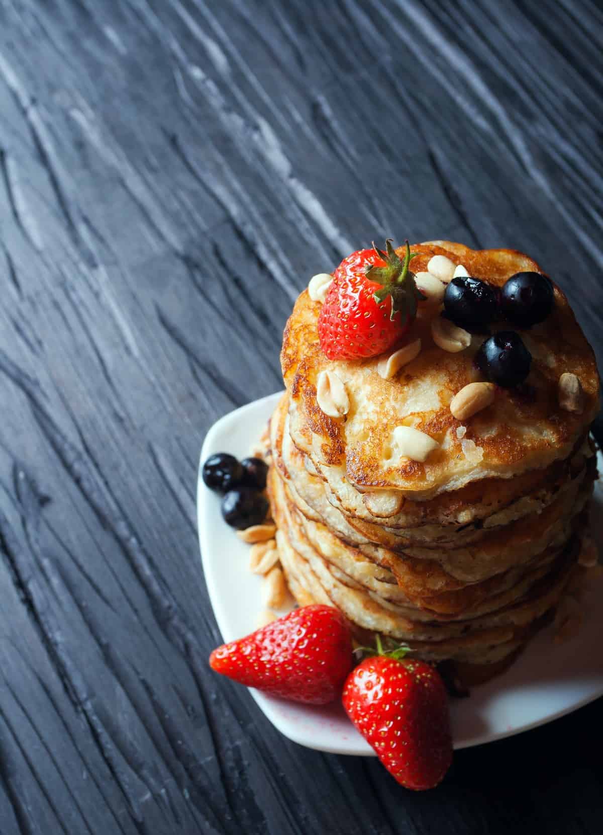 Large stack of pancakes with fruit.