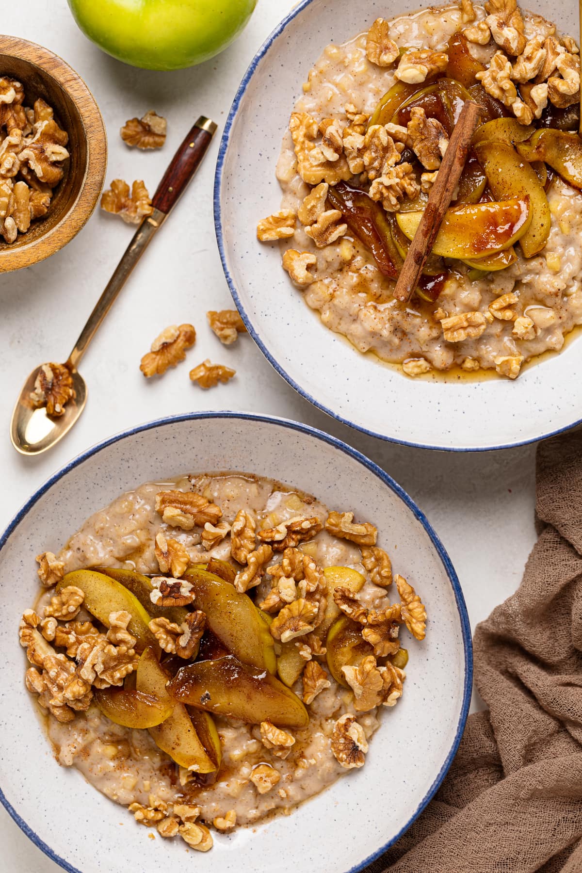 Two bowls of Apple Cinnamon Oatmeal Porridge topped with cinnamon sticks, nuts, and caramelized apples