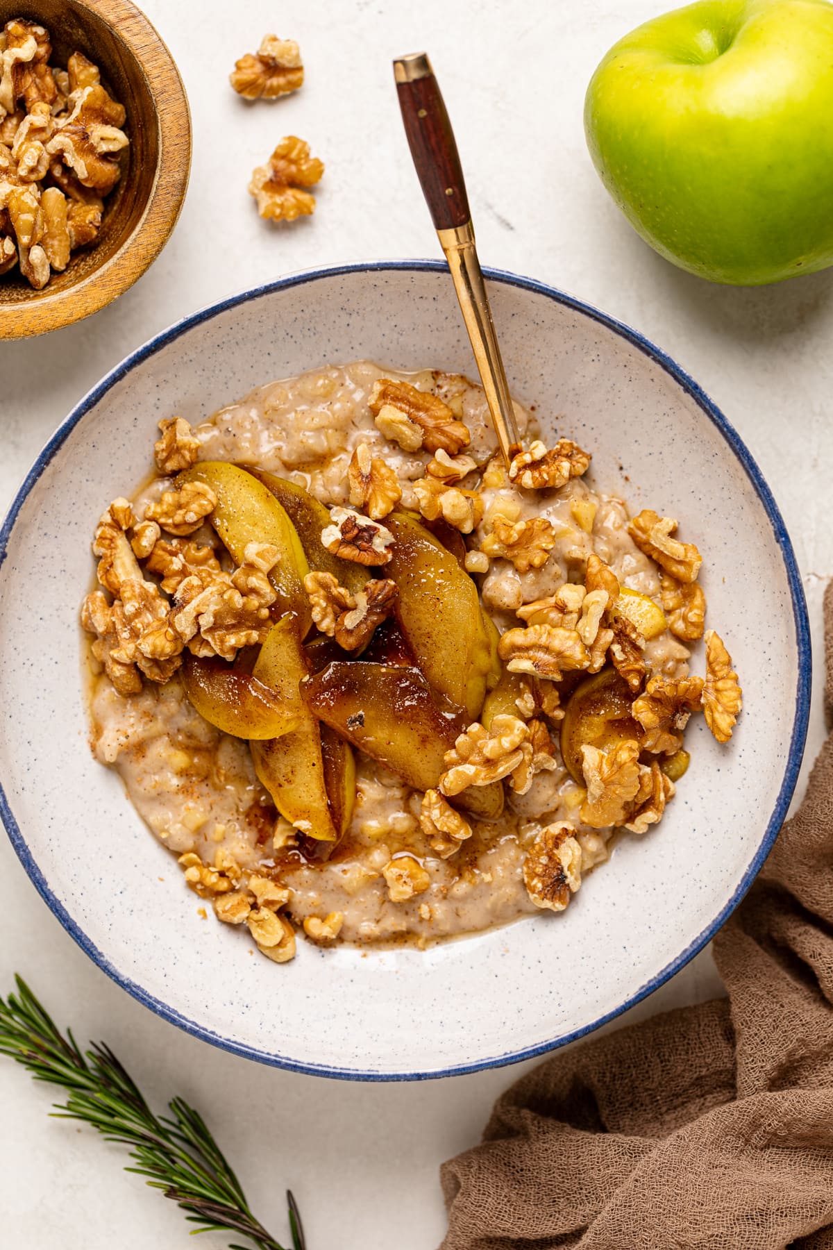 Spoon in a bowl of Apple Cinnamon Oatmeal Porridge topped with cinnamon sticks, nuts, and caramelized apples