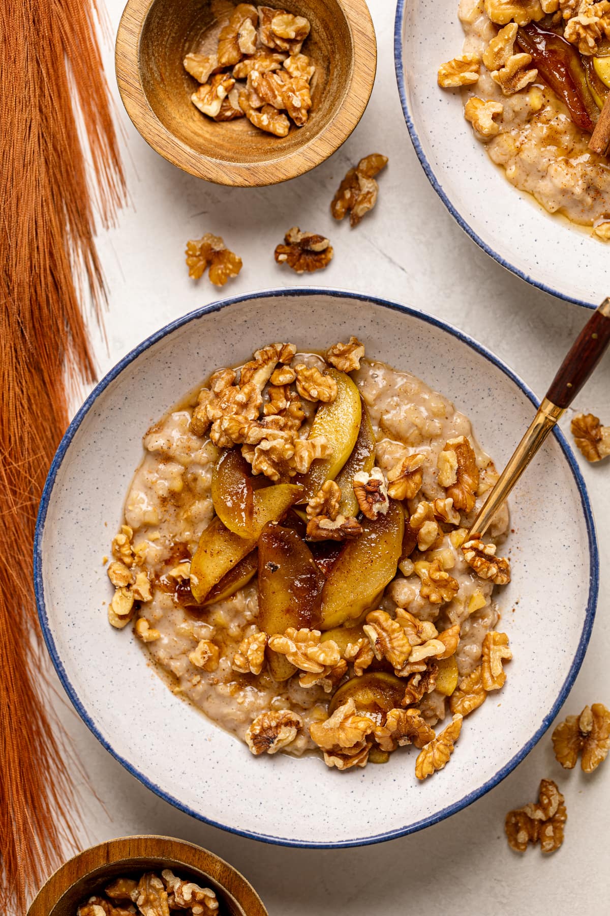 Spoon in a bowl of porridge topped with cinnamon sticks, nuts, and caramelized apples