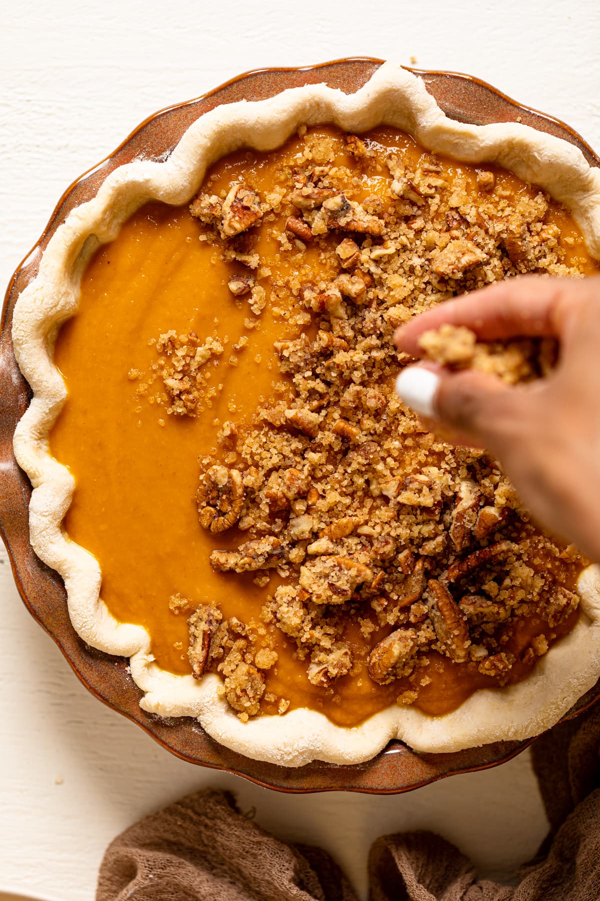 Hand adding crumble topping to an uncooked Vegan Maple Pumpkin Pie