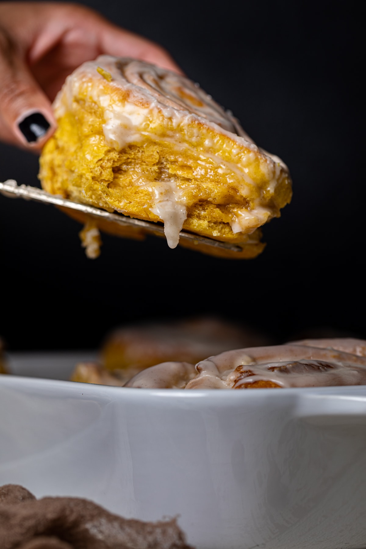 Woman removing a Vegan Pumpkin Cinnamon Roll from a baking dish with a spatula.