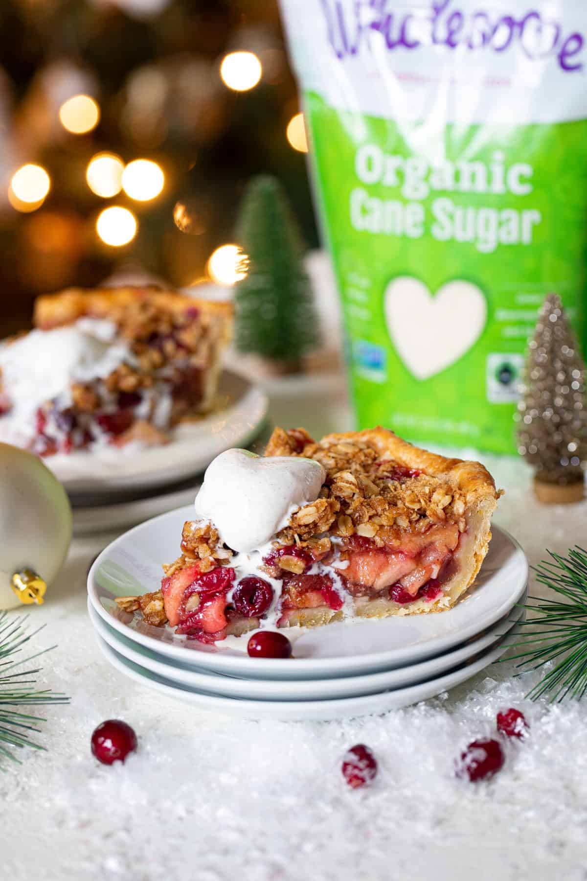 Slice of vegan apple cranberry crumble pie in front of a bag of organic cane sugar