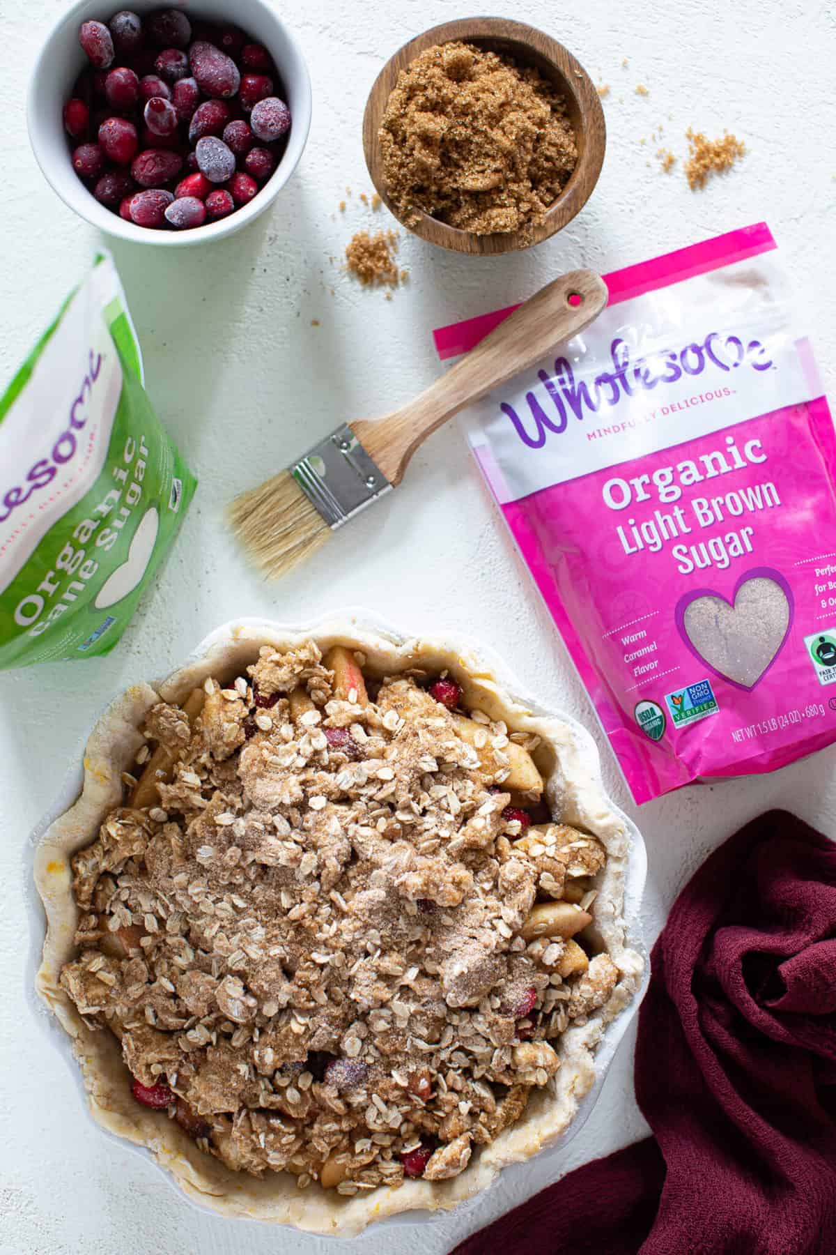 Overhead shot of Vegan Apple Cranberry Crumble Pie next to bags of organic cane and light brown sugar