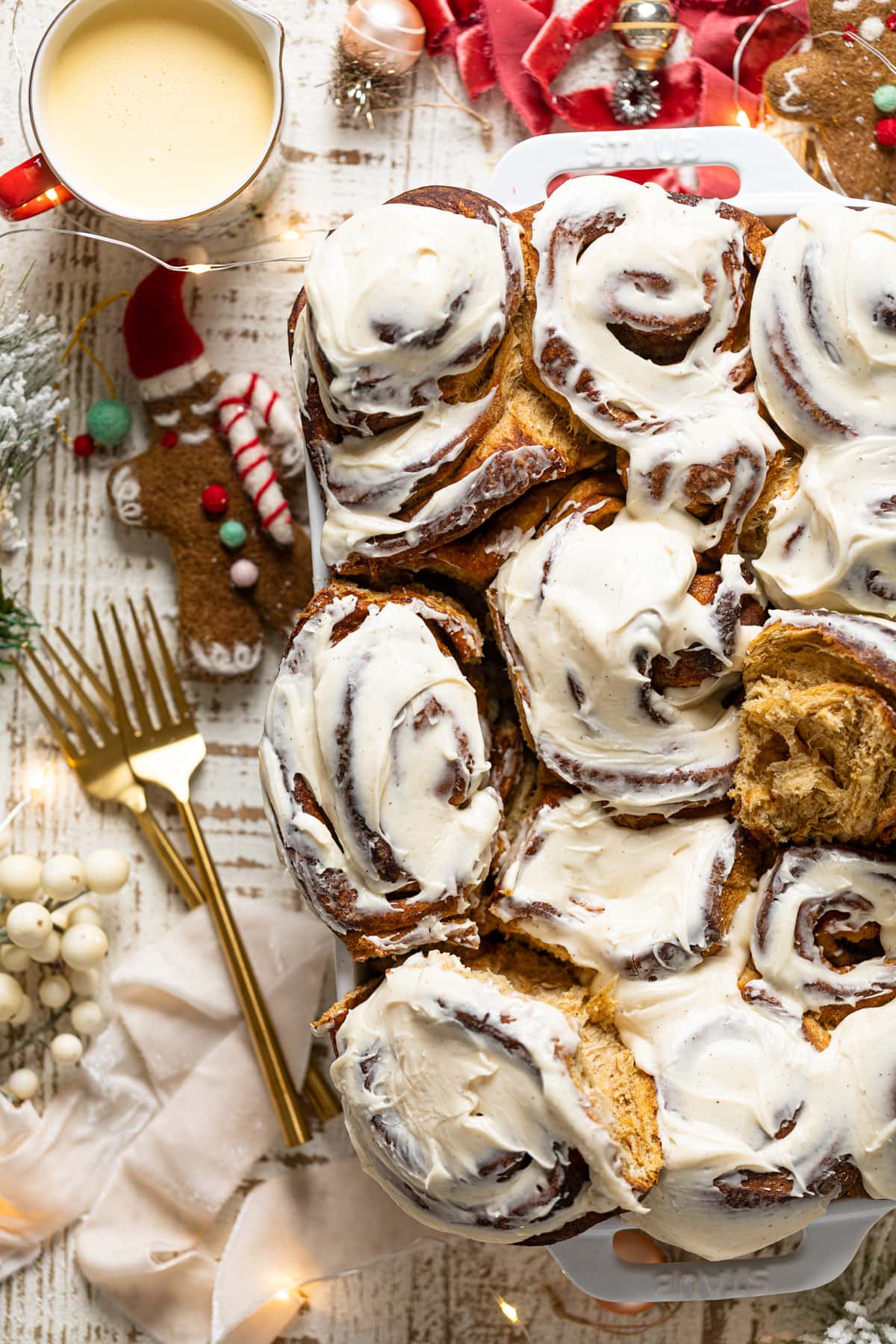 Gingerbread Cinnamon Rolls with Maple Cream Cheese Frosting in a baking dish surrounded by Christmas decorations and two forks