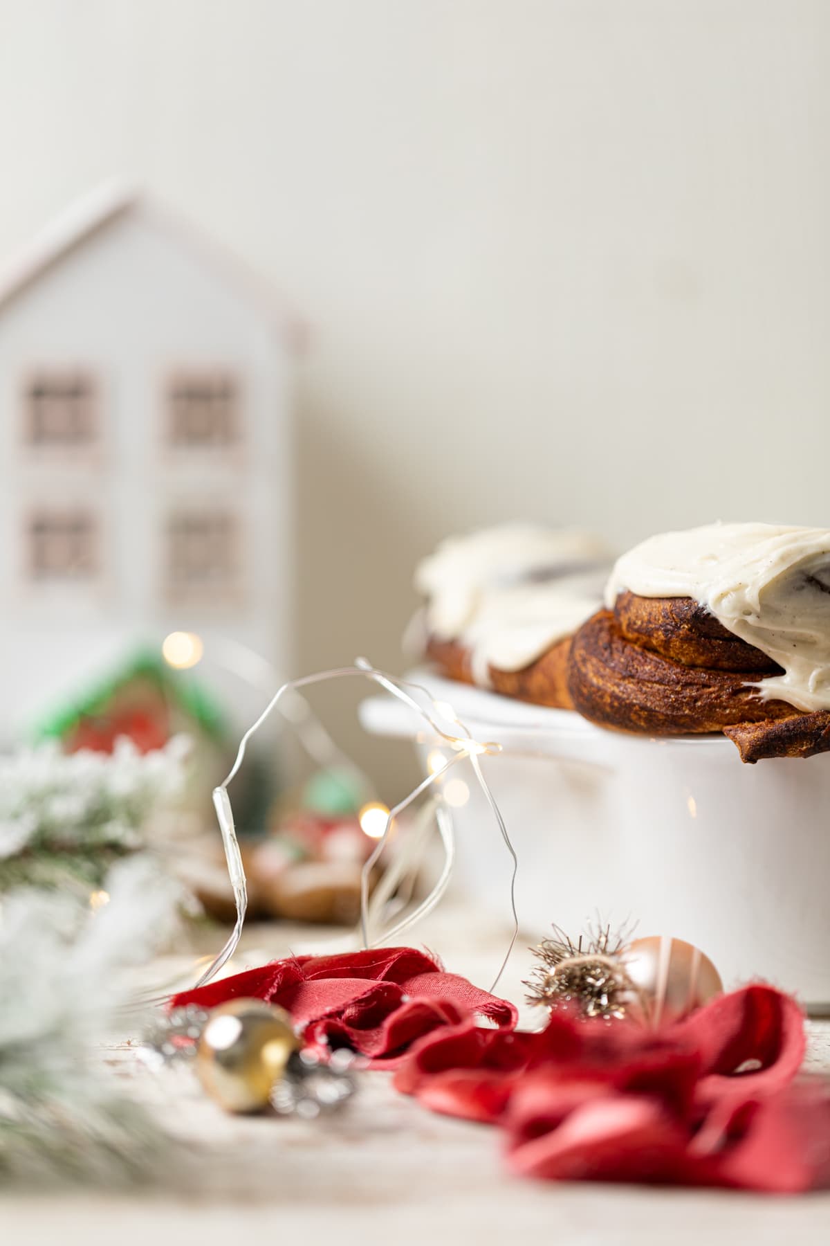 Gingerbread Cinnamon Rolls with Maple Cream Cheese Frosting on an elevated serving platform surrounded by Christmas decorations