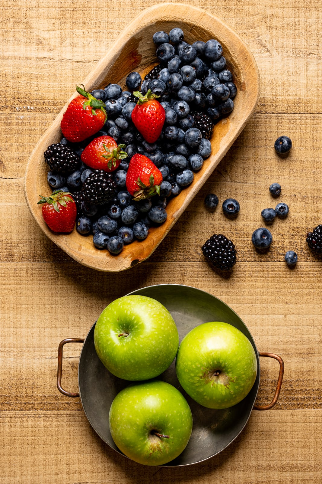 Bowls with fresh berries and green apples on a brown wood table.