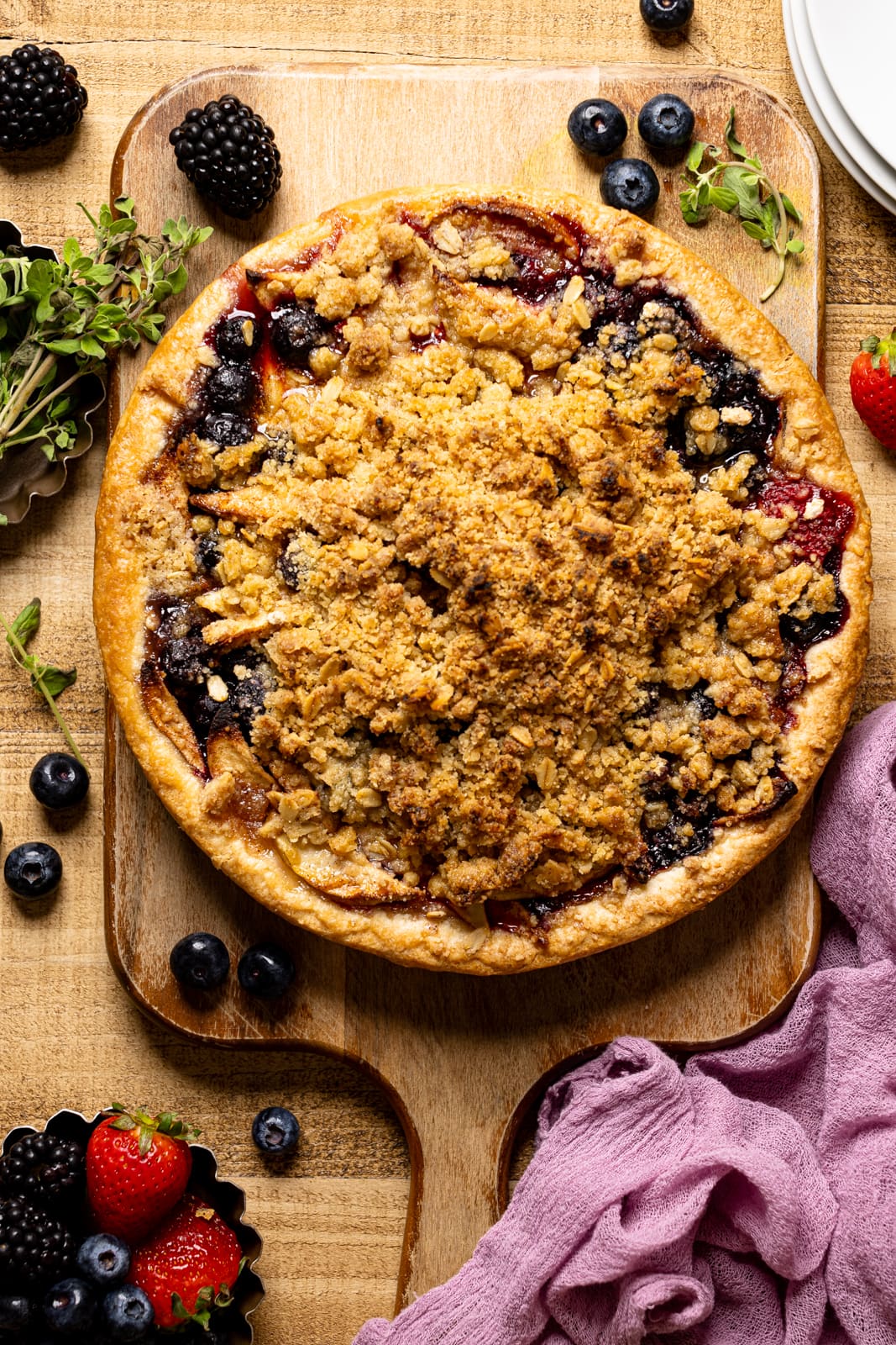 Whole pie on a brown wood table and a cutting board with fresh berries.