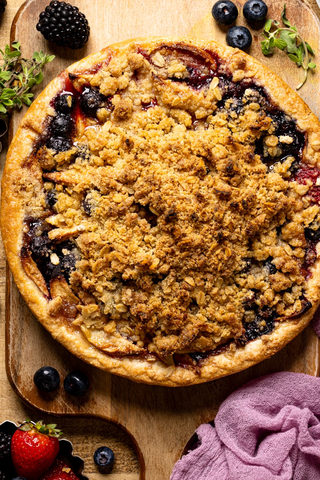Up close shot of whole baked pie on a cutting board on a brown wood table with fresh berries.