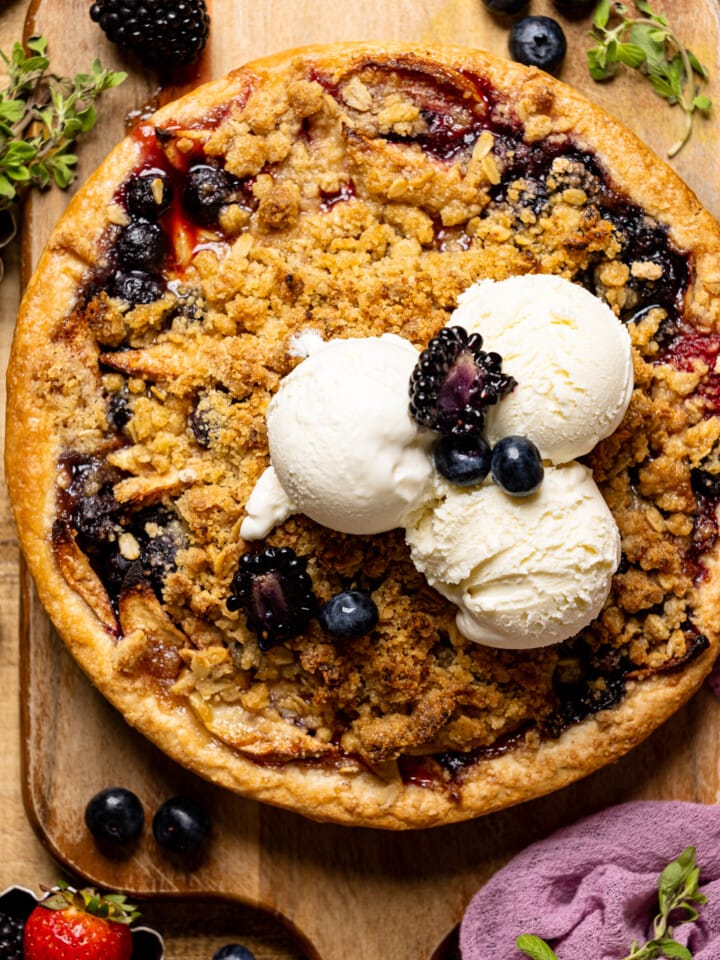 Baked whole pie on a cutting board on a brown wood table with fresh berries and scoops of ice cream.