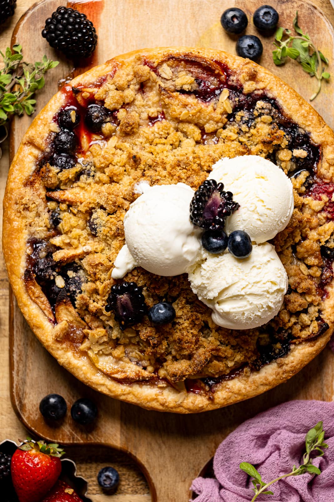 Baked whole pie on a cutting board on a brown wood table with fresh berries and scoops of ice cream.