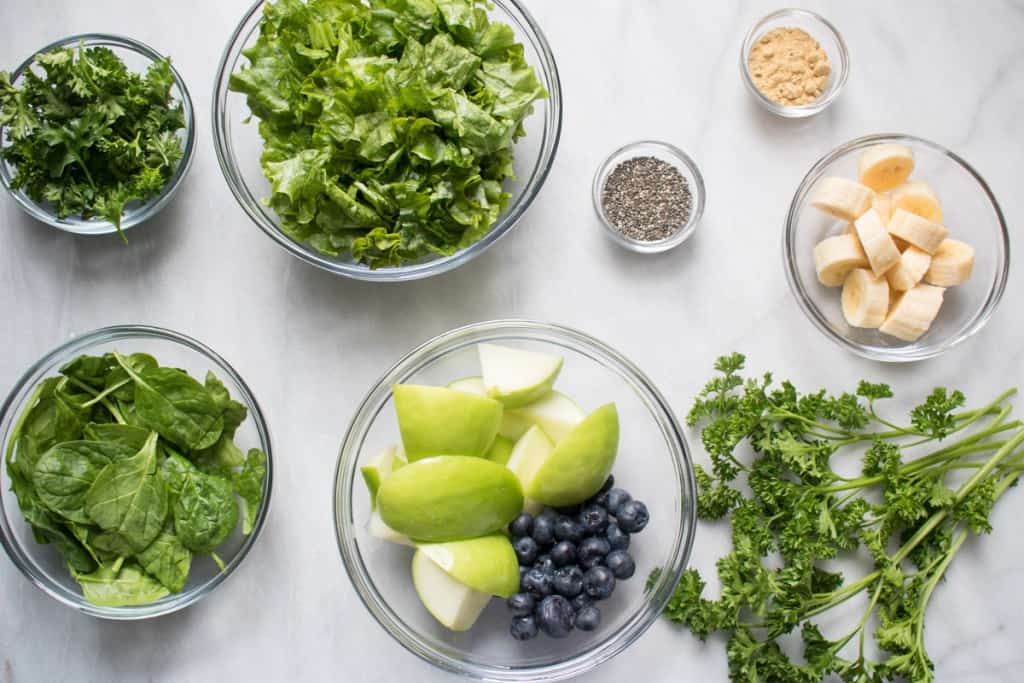 Bowls of ingredients including green apples, blue berries, and spinach.