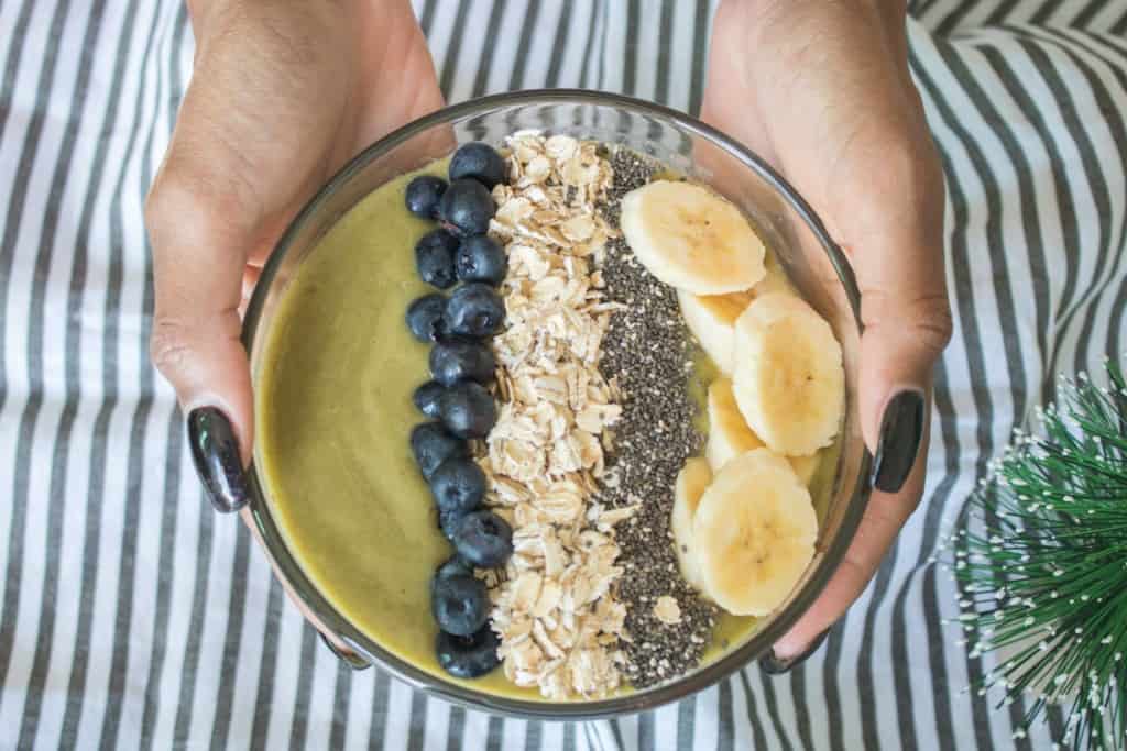 Woman holding a smoothie bowl topped with bananas, blueberries, chia seeds, and oats.