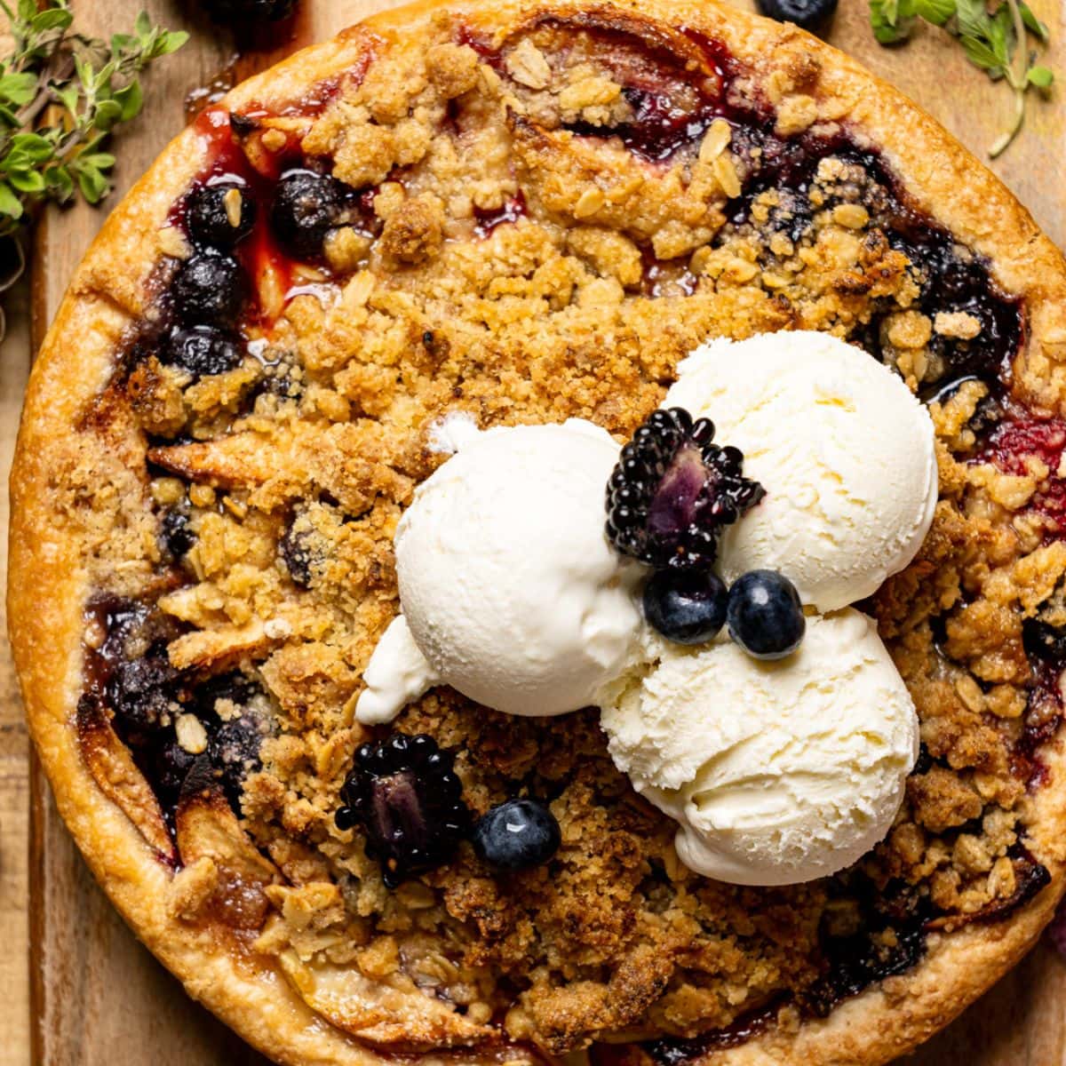 Baked whole pie on a cutting board on a brown wood table with fresh berries and scoops of ice cream.