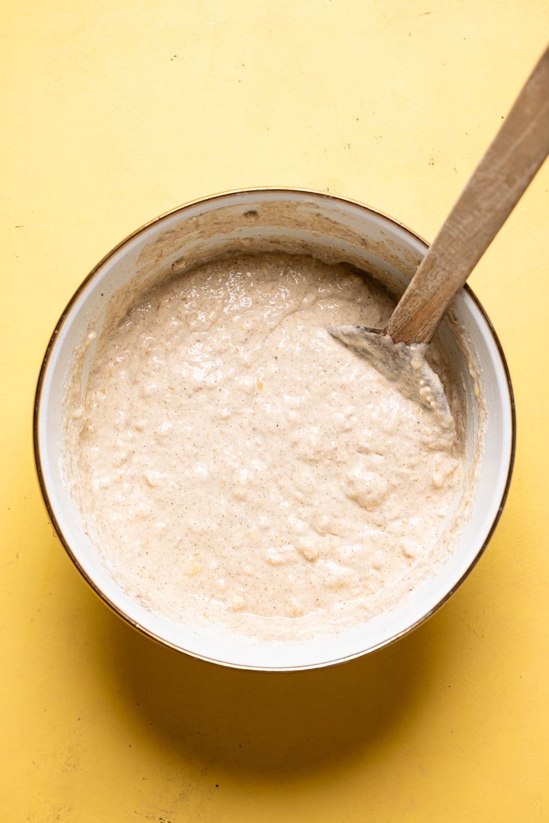 Pancake batter in a large white bowl with a wooden spoon.