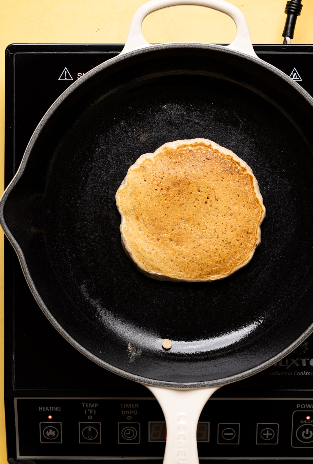 Pancake cooking in a skillet that is flipped. 